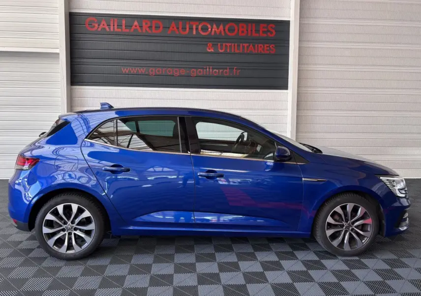 Profil côté gauche d'une Renault Mégane bleu 2023 garée en intérieur avec jantes alliage distinctives.