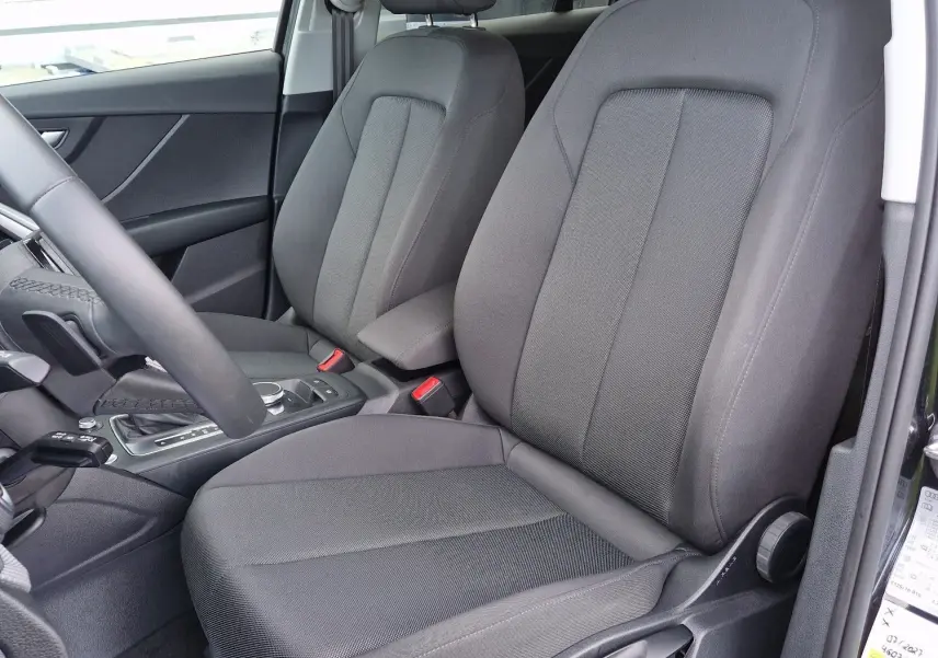 Vue intérieure côté conducteur de l'Audi Q2 35 TFSI 150CH en tissu noir, montrant les sièges avant et la console centrale.