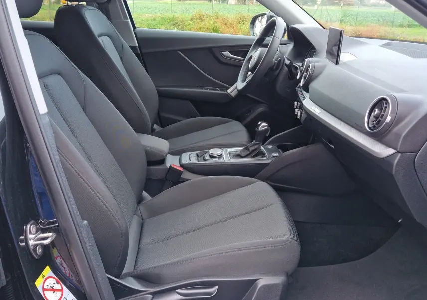 Intérieur côté conducteur de l'Audi Q2 noir mito metal 2023, montrant sièges tissu noir et tableau de bord moderne.