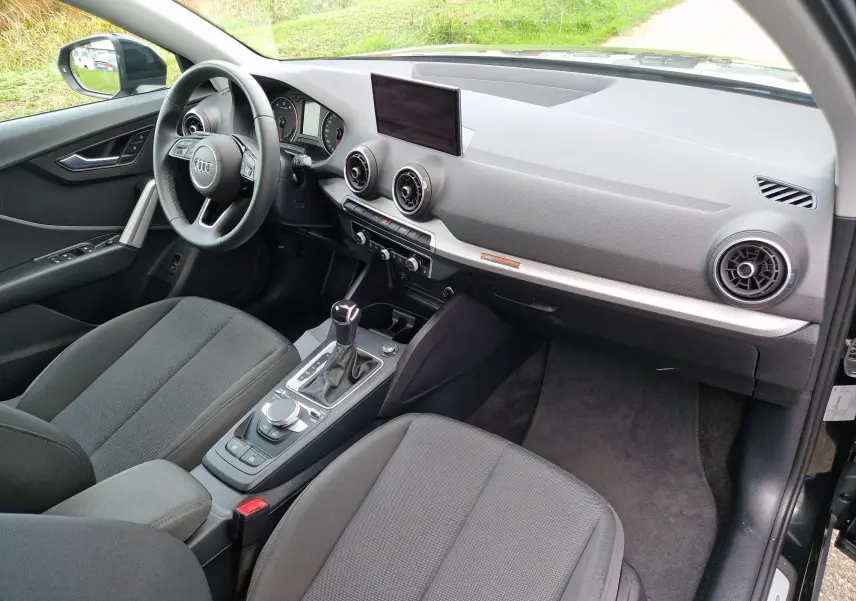 Intérieur côté conducteur de l'Audi Q2 noir mito metal 2023, avec tableau de bord moderne et écran central visible.