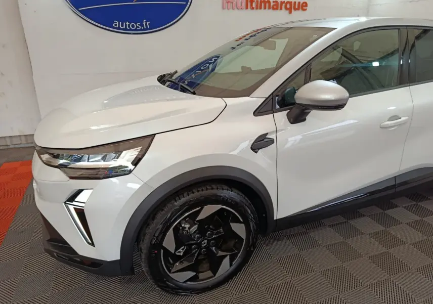 Vue de profil avant droit d'un Renault Captur blanc avec jantes noires et détails modernes sur l'aile avant.
