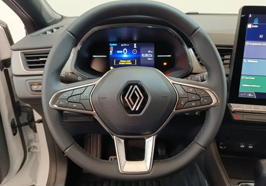 Vue rapprochée du volant cuir noir du Renault Captur blanc 2025 avec tableau de bord numérique et écran tactile central.