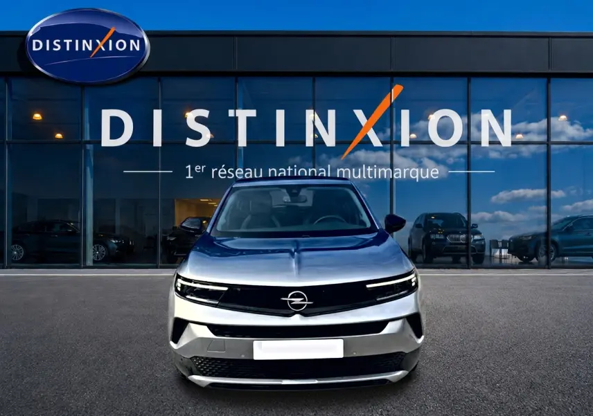 Opel Mokka gris 2025 vue de face, avec calandre noire et logo Opel centré devant un showroom Distinxion.