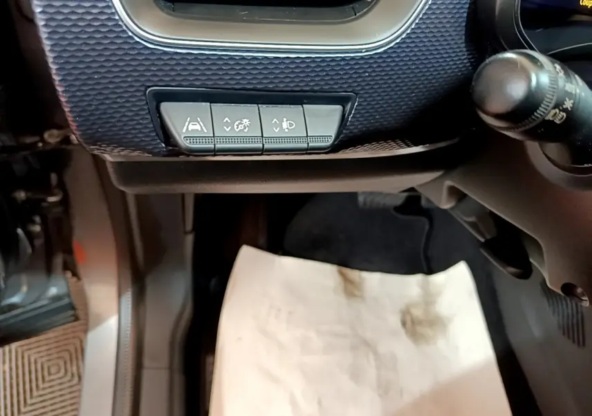 Gros plan sur les commandes sous le tableau de bord côté gauche d’un Renault Arkana gris foncé, avec pédalier et tapis de sol visible.