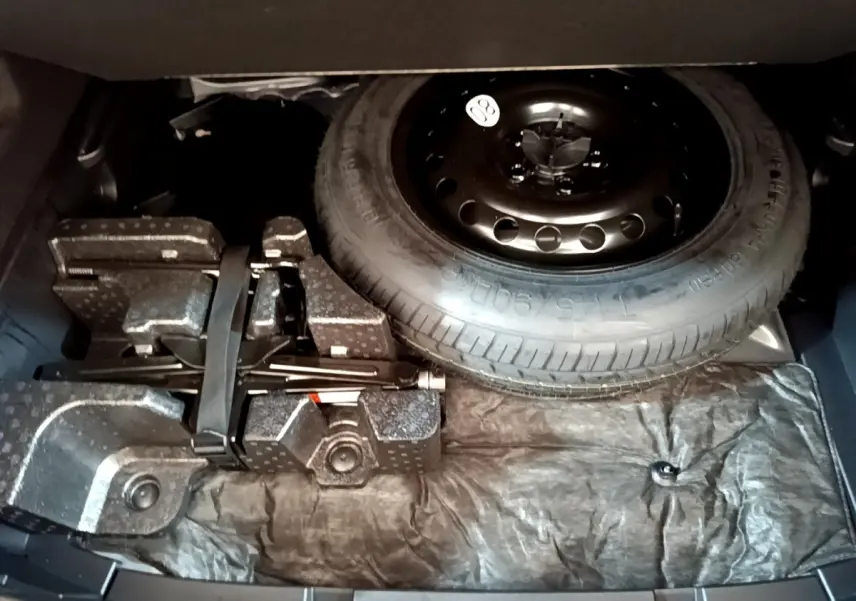 Vue du coffre ouvert d'une Renault Arkana Business E-TECH 145 2022, montrant la roue de secours et le kit de réparation.