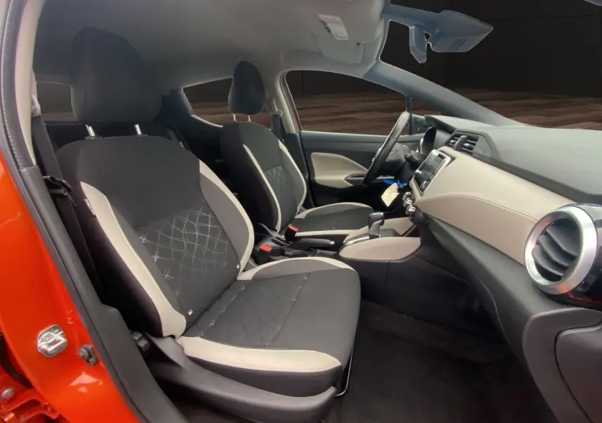 Vue intérieure côté gauche de la Nissan Micra orange Energy 2022, montrant les sièges tissu noir et beige et le tableau de bord clair.