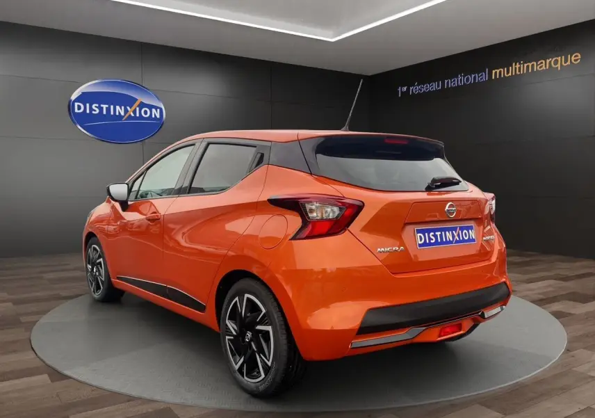 Vue 3/4 arrière droite d'une Nissan Micra 2022 orange Energy avec jantes noires et toit noir en showroom.