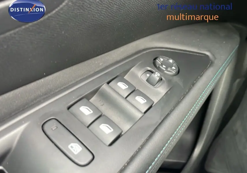 Gros plan sur les commandes de lève-vitres et rétroviseurs côté conducteur avec surpiqûres bleues sur la porte intérieure.