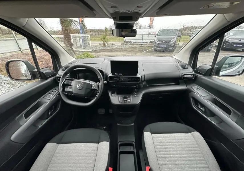 Vue intérieure avant du Citroën Berlingo 2025, montrant le tableau de bord noir et gris avec écran central et volant multifonction.