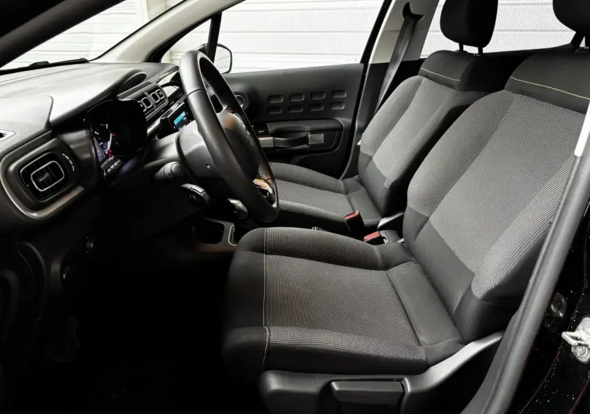 Vue intérieure côté conducteur de la Citroën C3 noire 2024, avec sièges tissu gris et tableau de bord moderne.