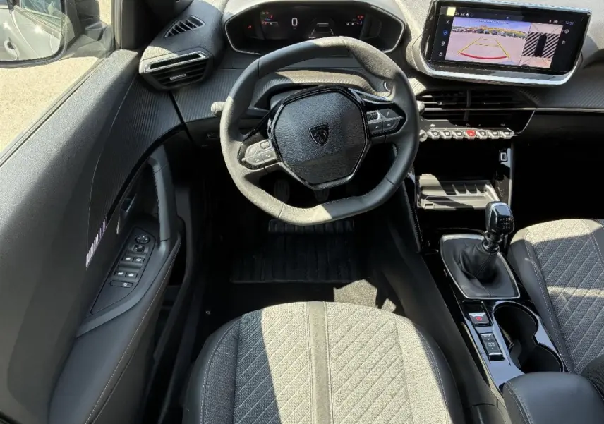 Vue intérieure avant du Peugeot 2008 2024, volant compact, écran tactile avec caméra de recul et levier de vitesse manuel.