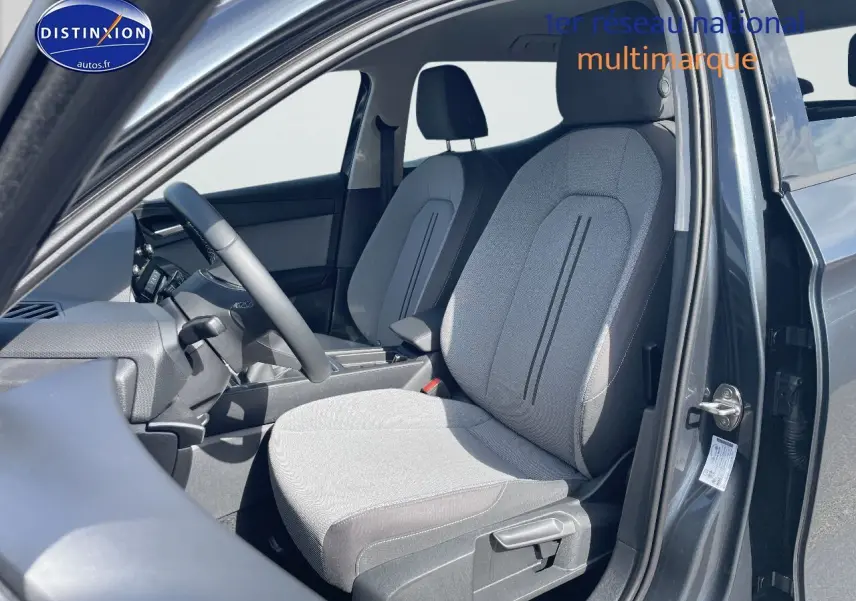 Vue intérieure côté conducteur de la SEAT LEON IV gris magnétique, mettant en valeur les sièges en tissu gris clair.