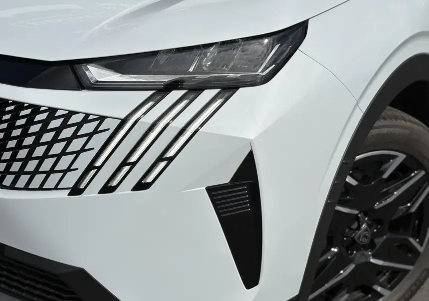 Gros plan sur l'avant droit blanc Okénite du Peugeot 5008 Hybrid 2025, mettant en valeur les feux LED griffés et la jante noire.