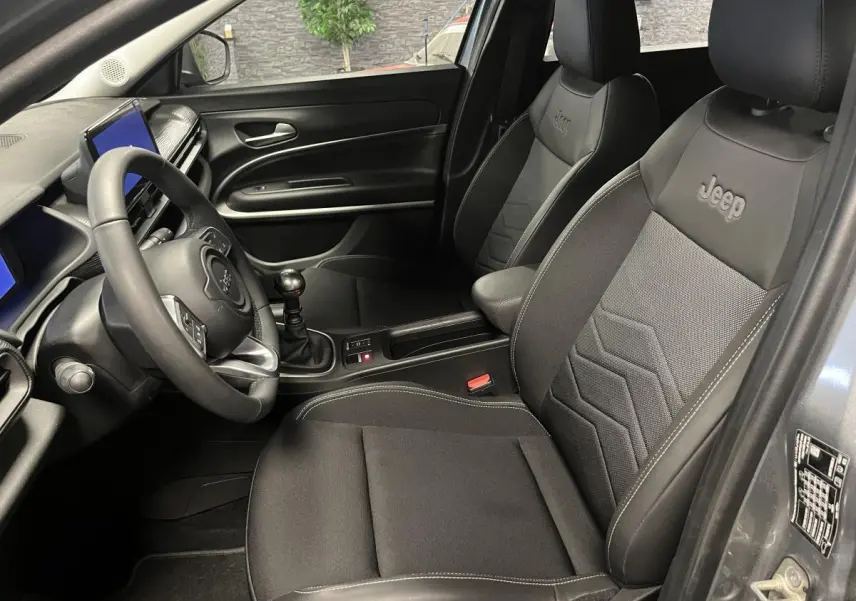 Vue intérieure côté conducteur du Jeep Avenger gris, mettant en valeur les sièges mixte tissu/TEP noir avec logo Jeep brodé.