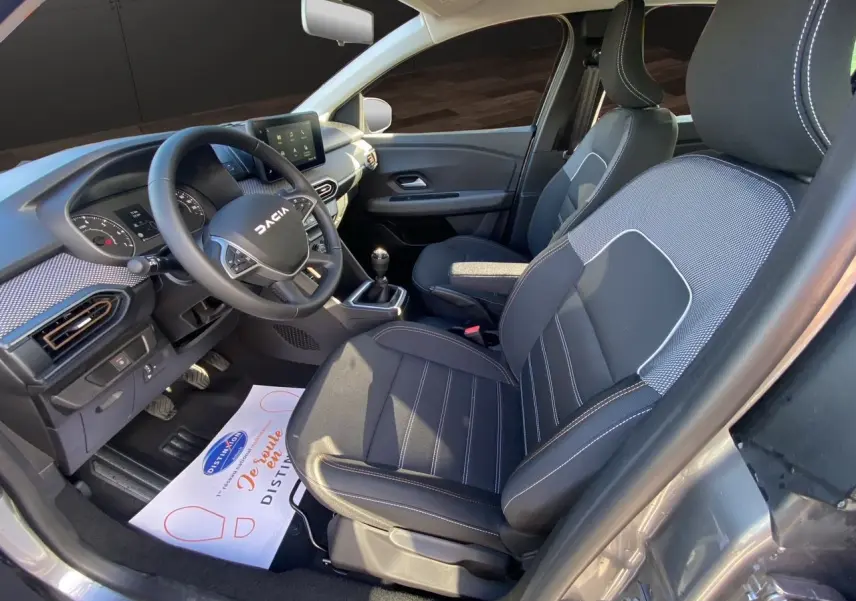 Intérieur côté conducteur de la Dacia Sandero Stepway gris schiste, volant multifonction et sièges tissu noir avec surpiqûres.
