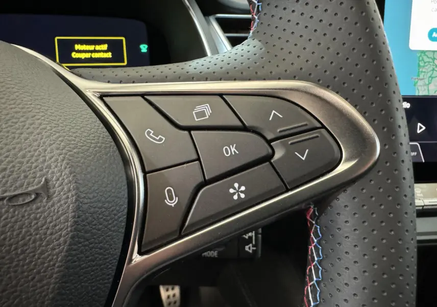 Gros plan sur les commandes multifonctions du volant perforé avec surpiqûres tricolores du Renault Captur blanc esprit Alpine E-Tech.