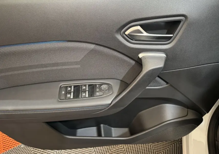 Gros plan sur la porte intérieure côté gauche du Renault Captur blanc, avec commandes de vitres et poignée noire.