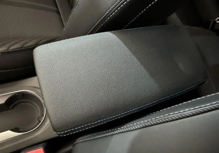 Gros plan sur l'accoudoir central noir avec surpiqûres bleues dans l'habitacle du Renault Captur blanc esprit Alpine E-Tech.