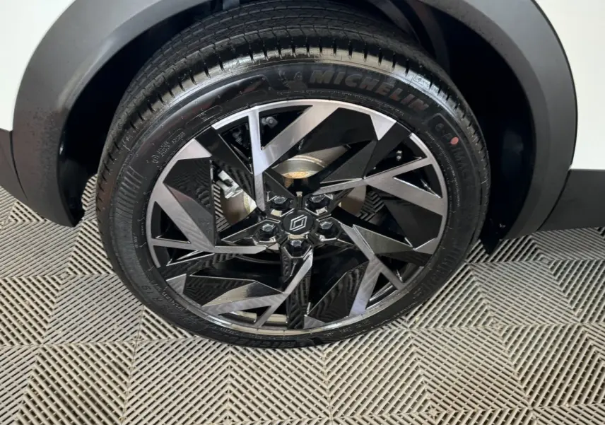 Gros plan sur la roue avant droite du Renault Captur blanc esprit Alpine E-Tech, jante alliage noire et argentée au design géométrique.