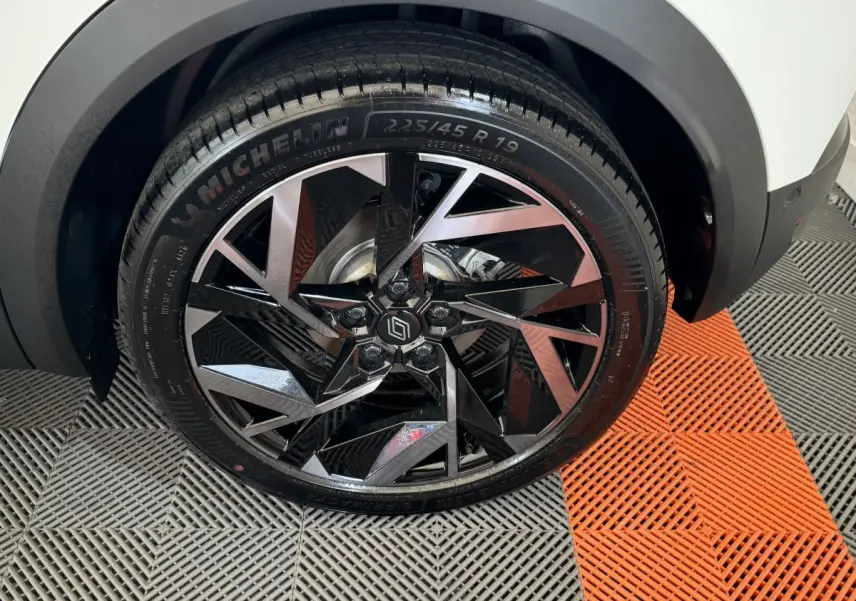 Gros plan sur la roue avant droite du Renault Captur blanc, mettant en valeur la jante noire et argentée au design géométrique.