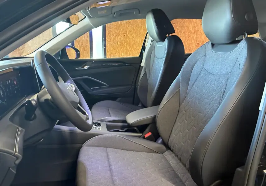 Vue intérieure côté gauche du Volkswagen Tiguan 2026, sièges tissu gris avec contours cuir noir et volant multifonction.