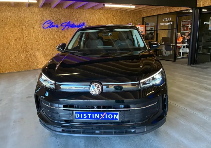 Vue avant d'un Volkswagen Tiguan noir grenadilla métallisé, avec calandre chromée et plaques Distinxion en intérieur showroom.