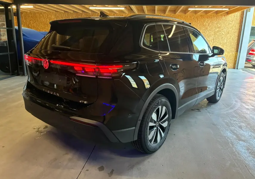 Vue 3/4 arrière droite du Volkswagen Tiguan noir Grenadilla Metal, avec feux arrière LED allumés dans un garage.