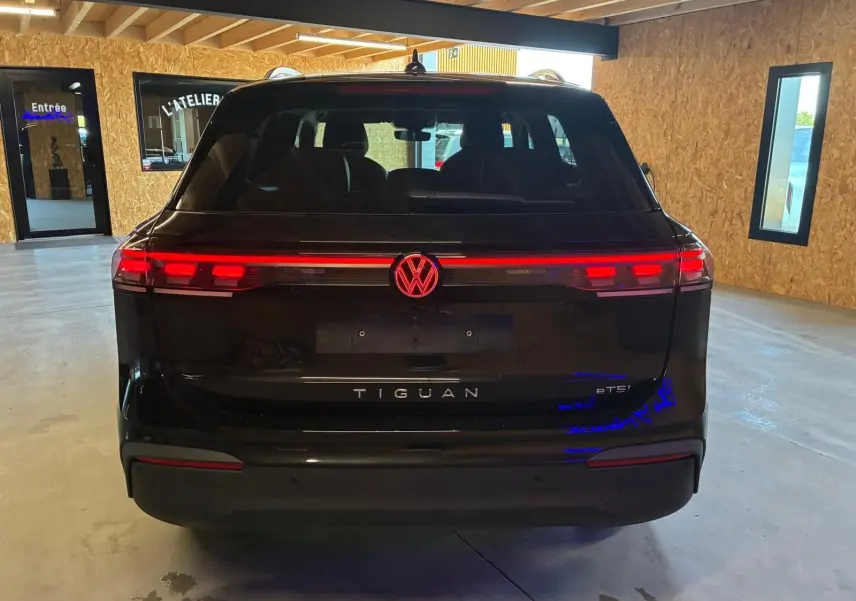 Vue arrière d'un Volkswagen Tiguan noir Grenadilla avec feux arrière LED allumés dans un garage.