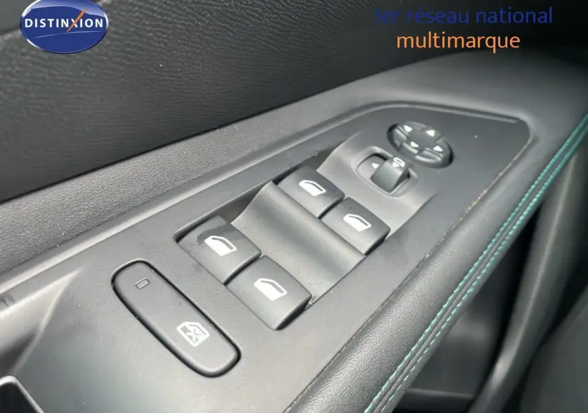 Gros plan sur les commandes de lève-vitres et rétroviseurs côté conducteur, garniture noire avec surpiqûres bleues.