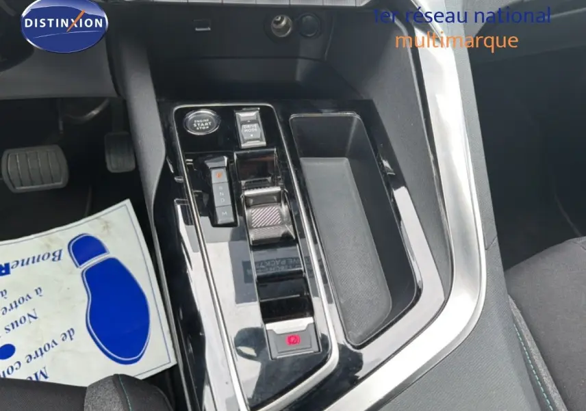 Gros plan sur la console centrale noire brillante du Peugeot 5008 bleu Celebes, avec levier de vitesses automatique et bouton start.