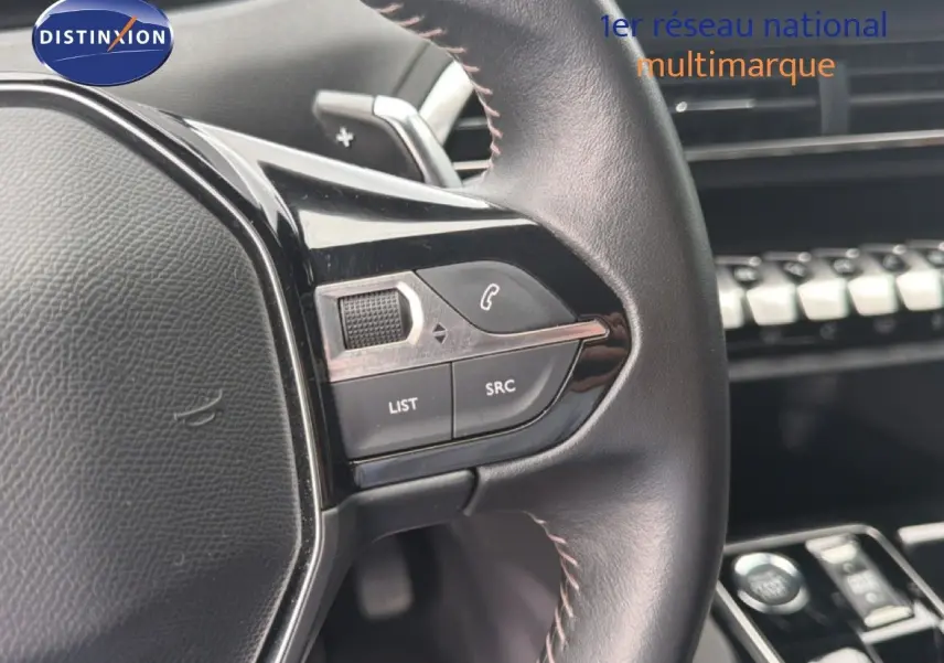 Gros plan sur le volant cuir noir du Peugeot 5008 bleu Célèbes, avec commandes intégrées et tableau de bord en arrière-plan.