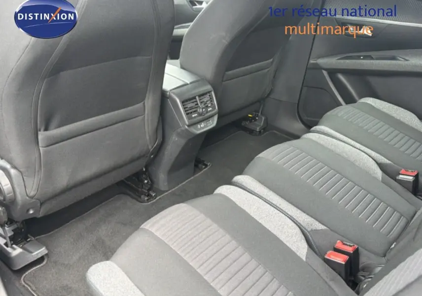 Vue intérieure arrière du Peugeot 5008 Hybrid 2024 montrant les sièges tissu gris et la console centrale avec aérateurs.