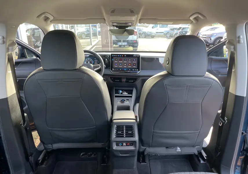 Vue intérieure arrière du Volkswagen Tiguan 2024 en Nightshade Blue, montrant les sièges avant en cuir noir et l'écran tactile central.