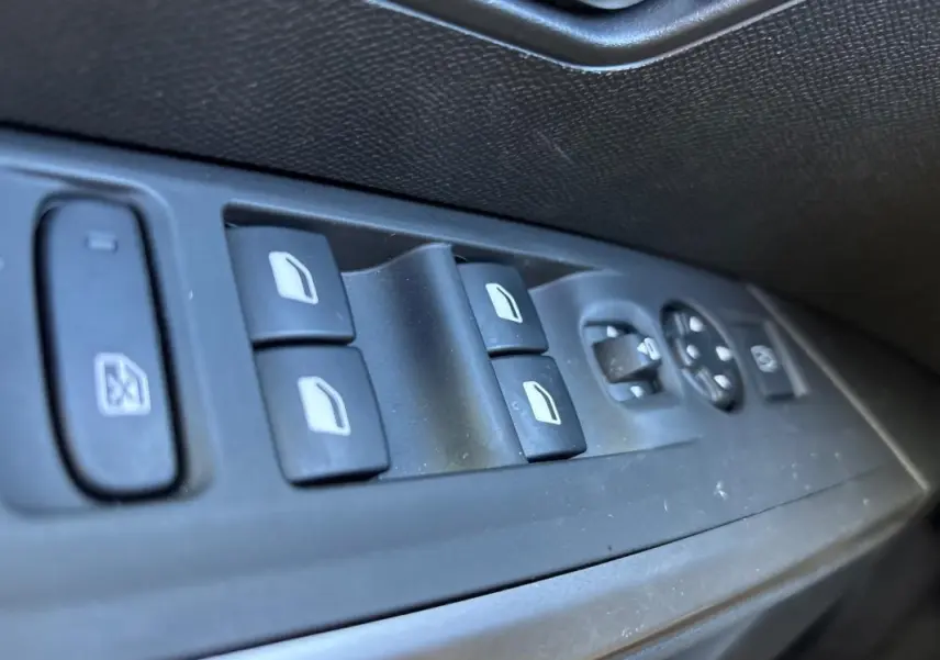 Gros plan sur les commandes des vitres électriques et rétroviseurs côté gauche d’un Peugeot 3008 gris Hybrid 145 e-DCS6 Allure.