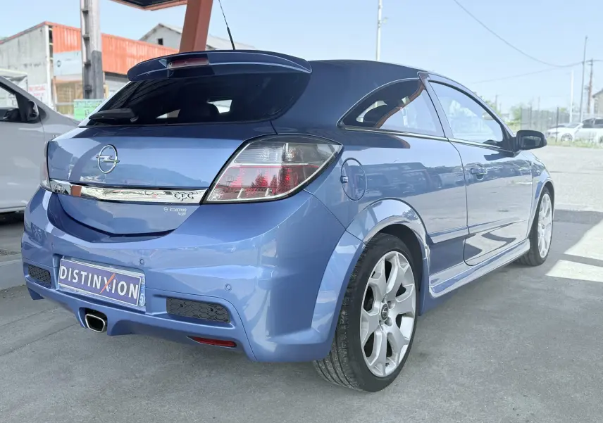 Vue 3/4 arrière droite d'une Opel Astra OPC bleue de 2008 avec jantes sport et aileron arrière distinctif.