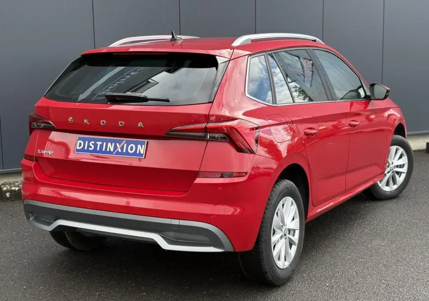 Vue 3/4 arrière droite d'un Skoda Kamiq 2024 rouge Velvet avec jantes alliage et barres de toit alu.