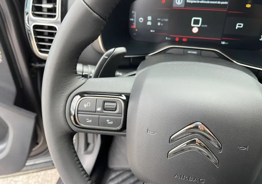 Gros plan sur le volant noir du Citroën C5 Aircross Hybrid 145, avec commandes intégrées et tableau de bord numérique visible.