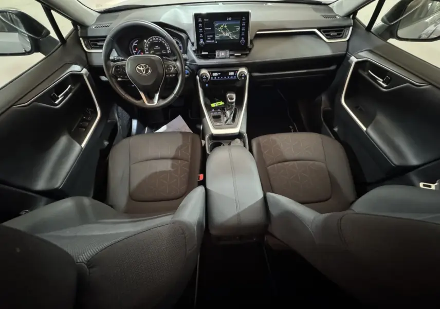 Vue intérieure avant du Toyota RAV4 hybride 2021 avec tableau de bord moderne, écran tactile et sièges noirs en tissu.