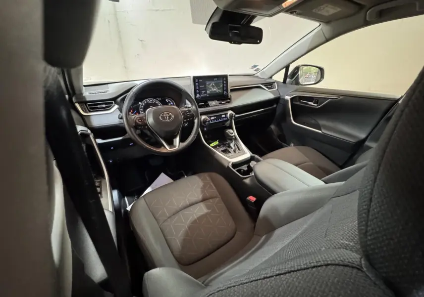 Intérieur Toyota RAV4 hybride 2021 vu côté conducteur, sièges noirs et tableau de bord avec écran tactile central.