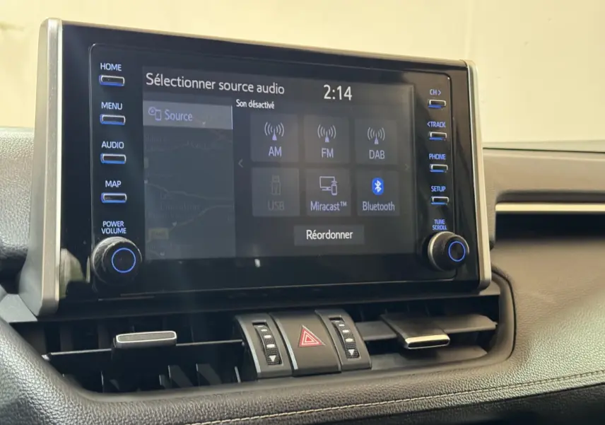 Écran tactile central du Toyota RAV4 hybride 2021, vue rapprochée du tableau de bord noir avec commandes audio visibles.