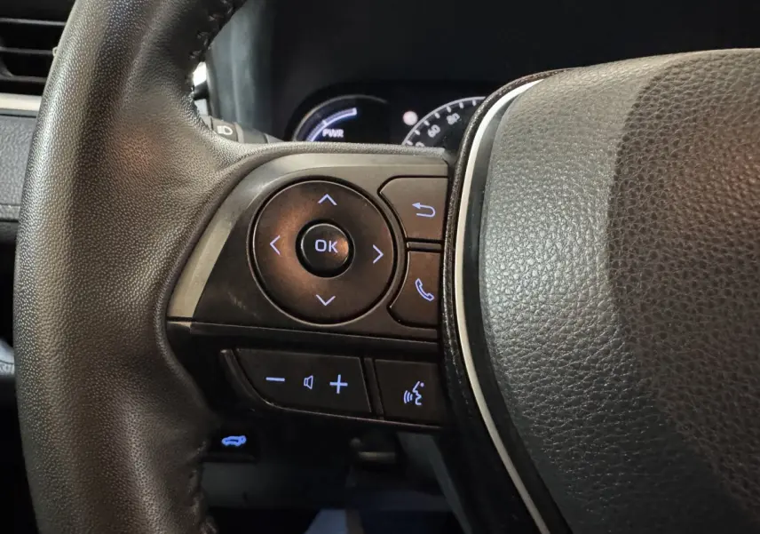 Gros plan sur les commandes du volant cuir noir du Toyota RAV4 hybride 2021, avec boutons rétroéclairés bleus.