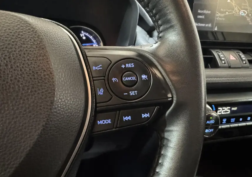 Gros plan sur le volant cuir noir côté droit du Toyota RAV4 hybride 2021 avec commandes de régulateur et multimédia éclairées.