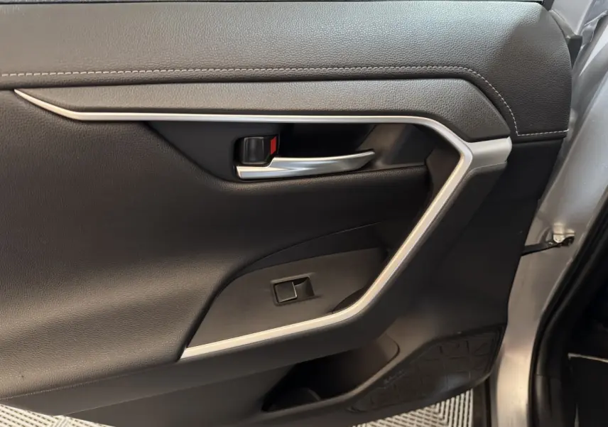 Gros plan sur la porte intérieure côté droit du Toyota RAV4 gris clair, avec poignée argentée et garniture noire.