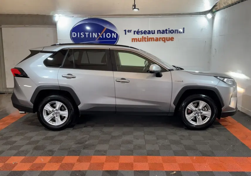 Profil droit d'un Toyota RAV4 hybride gris clair 2021, avec jantes alliage et logo Distinxion en arrière-plan.