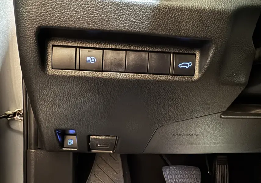 Gros plan sur les commandes noires sous le tableau de bord du Toyota RAV4 gris clair, avec bouton ouverture coffre éclairé.