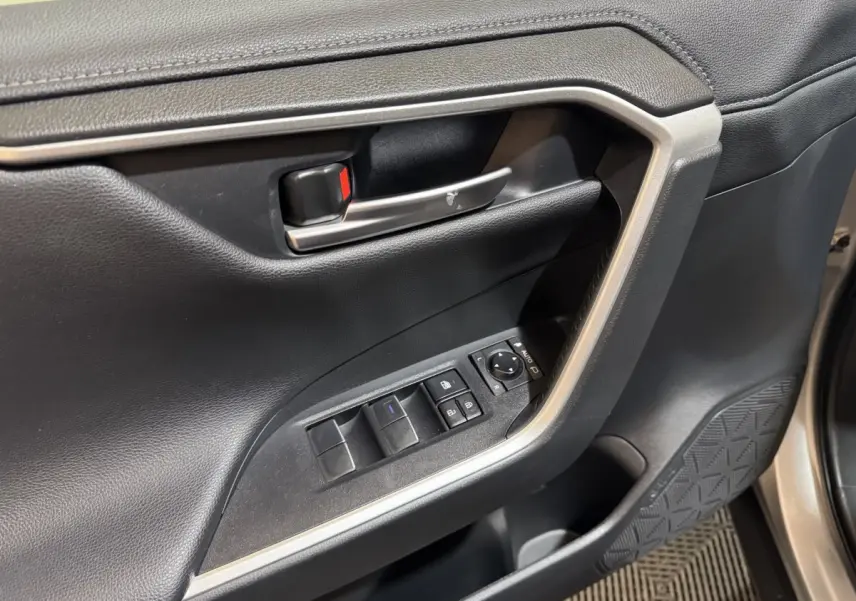 Gros plan sur la porte intérieure côté conducteur du Toyota RAV4 gris clair, avec commandes de vitres et rétroviseurs.