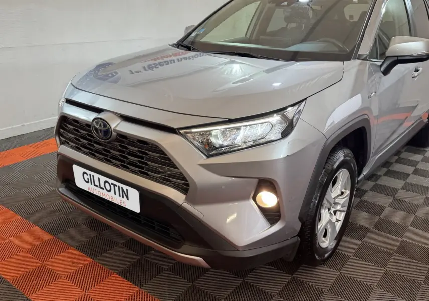 Vue 3/4 avant droit d'un Toyota RAV4 gris clair hybride avec phares LED et antibrouillards allumés.