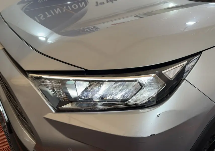 Gros plan sur le phare avant droit du Toyota RAV4 hybride gris clair, soulignant les lignes modernes et les LED distinctives.