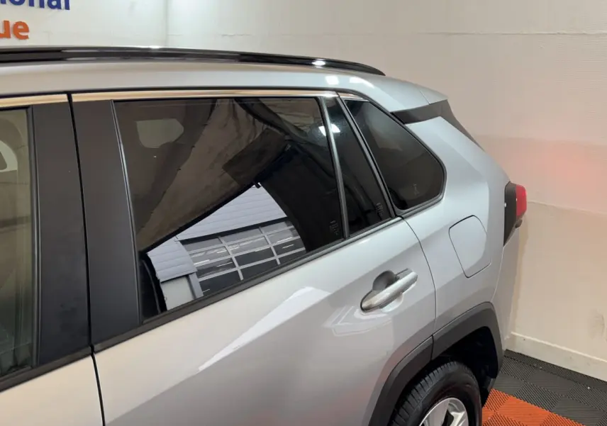 Vue côté arrière droit du Toyota RAV4 hybride gris clair, mettant en valeur la porte arrière et la roue.