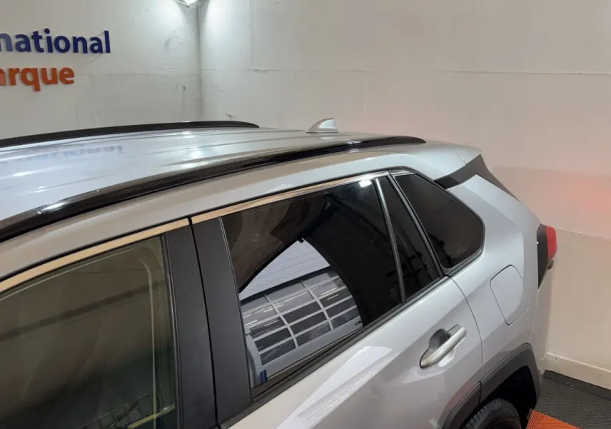 Vue latérale droite d'un Toyota RAV4 gris clair 2021 avec barres de toit noires et vitres teintées.